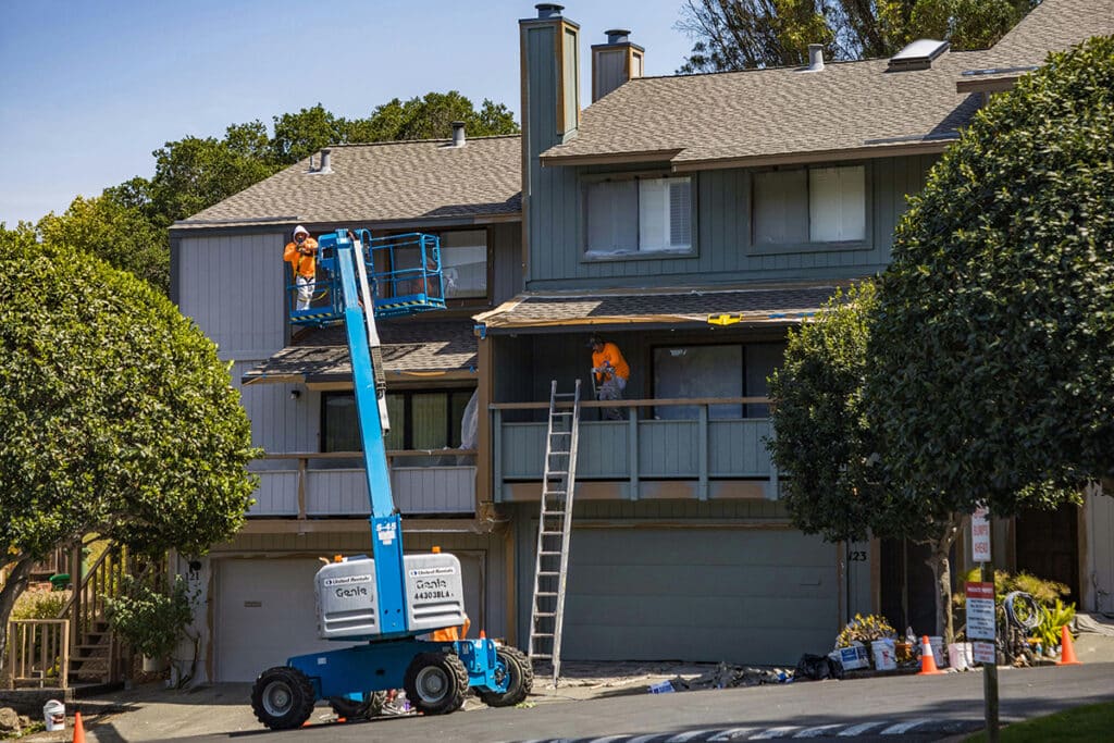 Workers using a lift and ladder to install roofing, demonstrating efficient roofing project management.