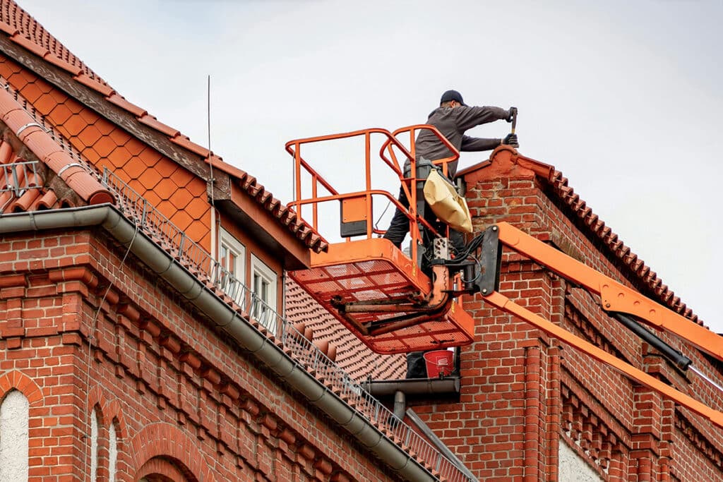 Worker on a lift repairing a roof, showing why marketing roofing business needs strong project photos.