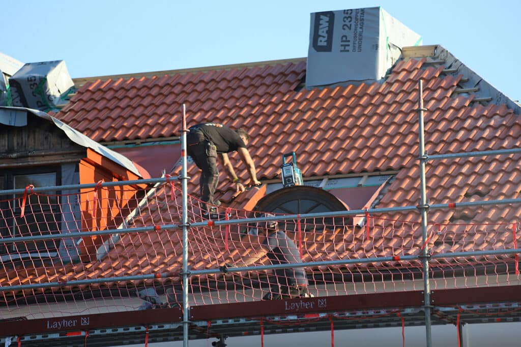 Worker on scaffolding performing tasks with aerial roof measurements technology in use.