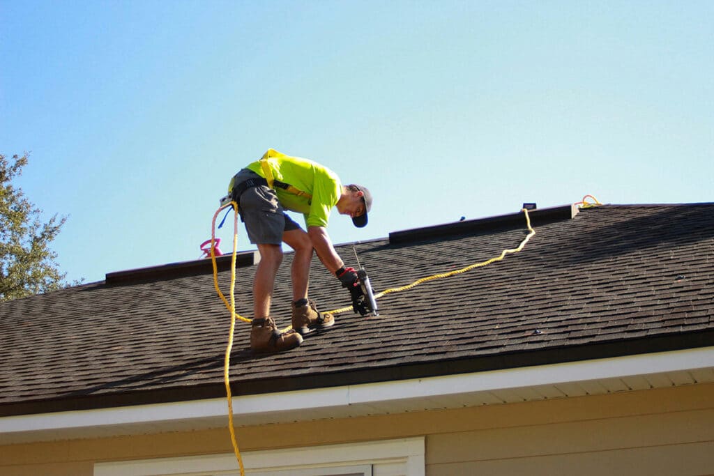 Expert applying shingles on a roof while using safety gear, as part of a job involving roofing quotes.